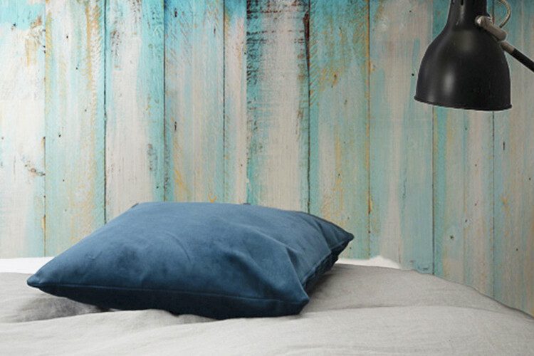 Lit avec coussin et mur décoré d'un papier peint bleu à motifs de grain de bois d'aspect vintage.