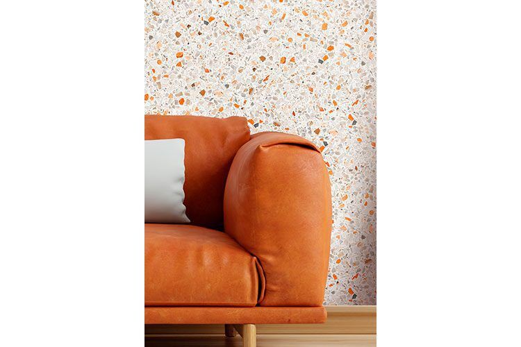 Sofa naranja y al fondo pared con papel pintado con motivo impreso que simula el terrazo en tonos naranjas.